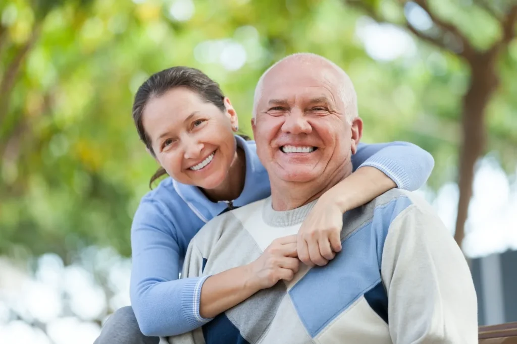 Smiling senior couple outdoors with dental implants for seniors improved oral health